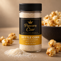 Popcorn Czar Kettle Corn popcorn seasoning in a 2 oz round shaker with a gold flavour band, shown with caramel-coloured kettle corn and a bowl of popcorn