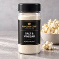 Product visualization of Popcorn Czar Salt & Vinegar in a round 2 oz shaker with a black-and-gold label beside seasoned popcorn. Actual batch shade may vary.