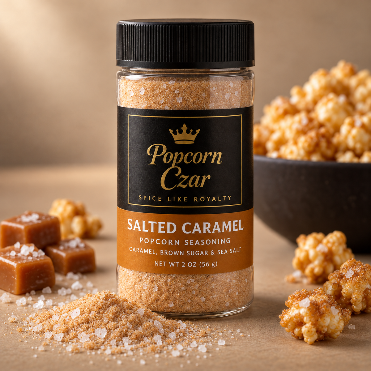 Popcorn Czar Salted Caramel popcorn seasoning in a 2 oz round shaker with an amber flavour band, shown with caramel pieces, flaky sea salt and a bowl of popcorn