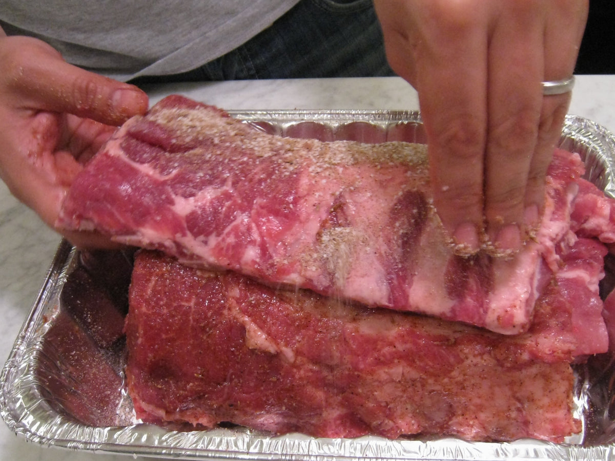 Dry spice rub being applied to pork ribs, representing Spice Czar All American Dry Rub. Photo by Daryn Nakhuda via Wikimedia Commons, CC BY 2.0.