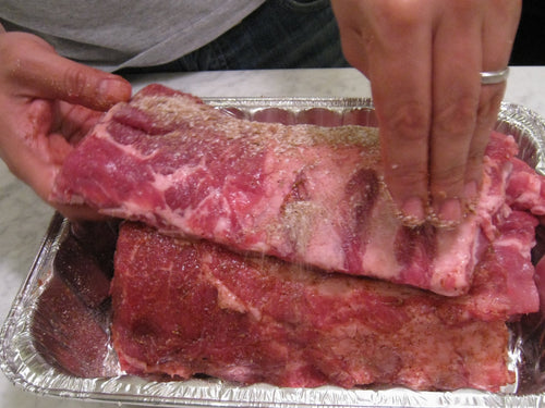 Dry spice rub being applied to pork ribs, representing Spice Czar All American Dry Rub. Photo by Daryn Nakhuda via Wikimedia Commons, CC BY 2.0.