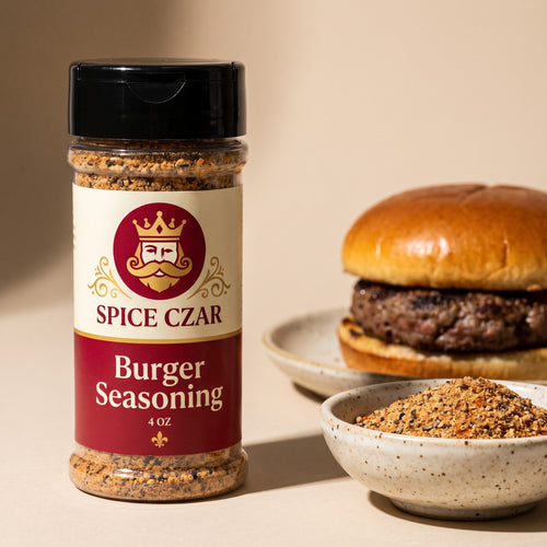 Spice Czar Burger Seasoning 4 oz shaker beside a speckled bowl of the coarse tan blend flecked with black pepper and smoked paprika, with a grilled hamburger on a brioche bun behind