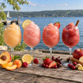 AI-generated serving suggestion for the Finger Lakes Pour Flight: four peach, lemon-raspberry, pink berry and spiced cranberry-apple slushies in wine glasses beside a lake. Drinks, fruit and glassware not included.